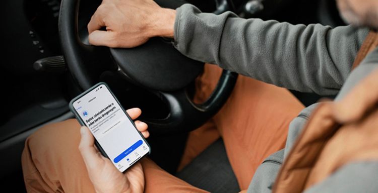 Osoba w samochodzie trzymająca smartfon z otwartą aplikacją mobilną